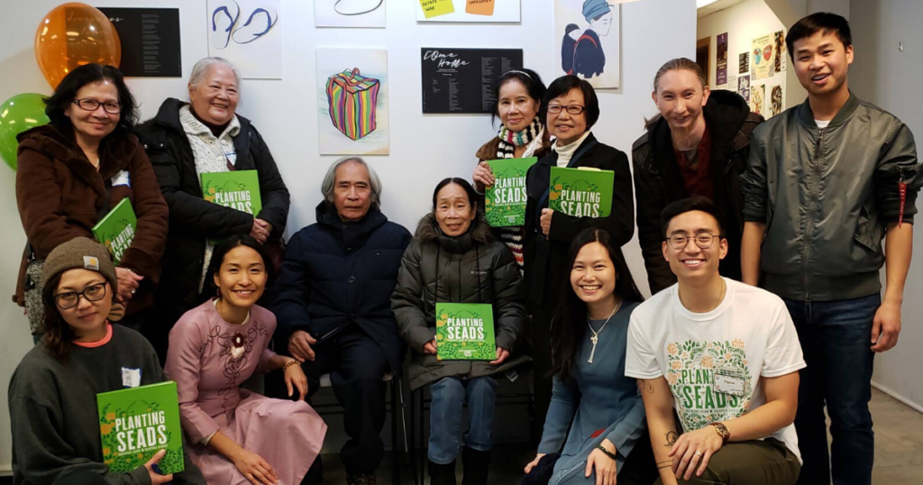 A group of Southeast Asian Americans of varying ages face the camera smiling. Many hold a green book titled "Planting SEADS: Southeast Asian Diaspora Stories."