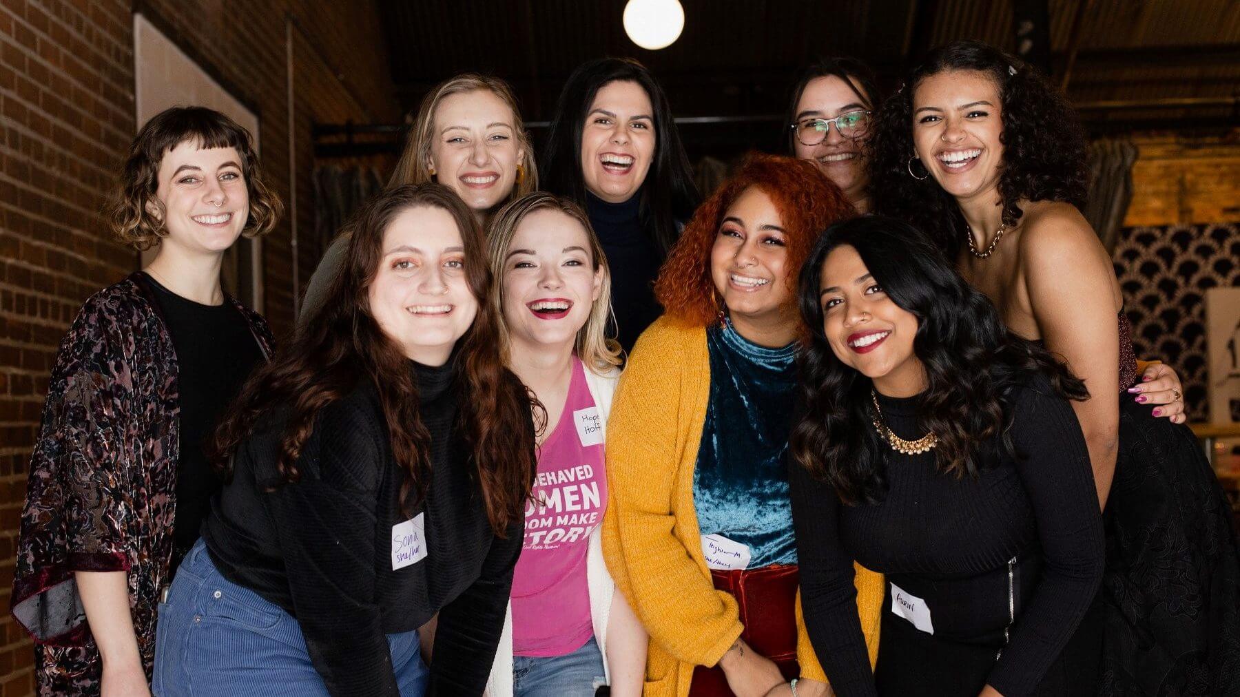 A group of young women smile together with a light overhead