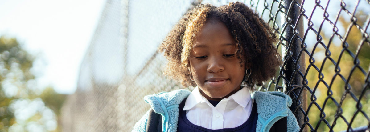 girl outside standing in front of fence looking down at her phone